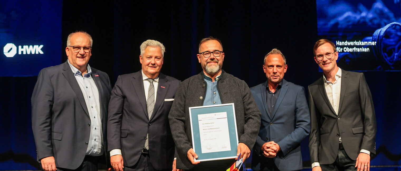 Jungmeister Matthias Wölfel präsentiert seine Ehrenurkunde mit Gratulanten auf der Bühne.