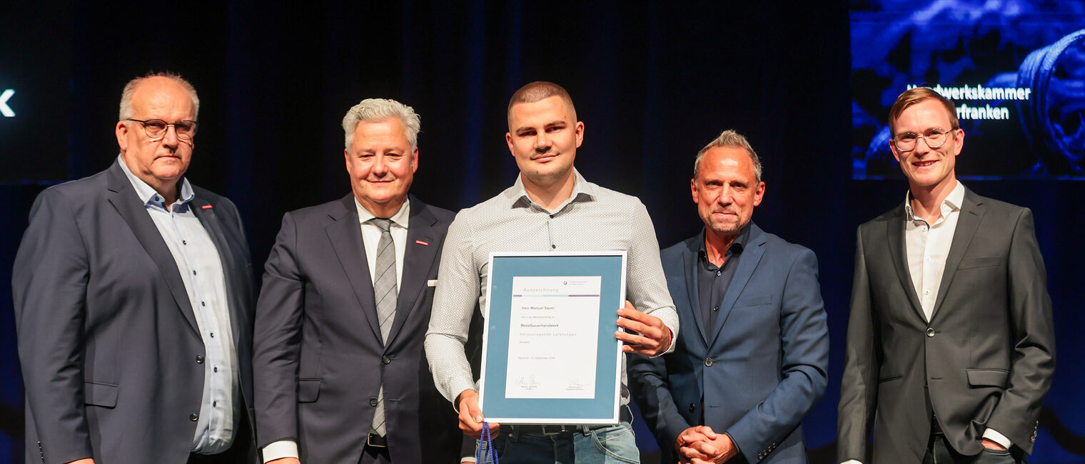 Jungmeister Manuel Sauer präsentiert seine Ehrenurkunde mit Gratulanten auf der Bühne.