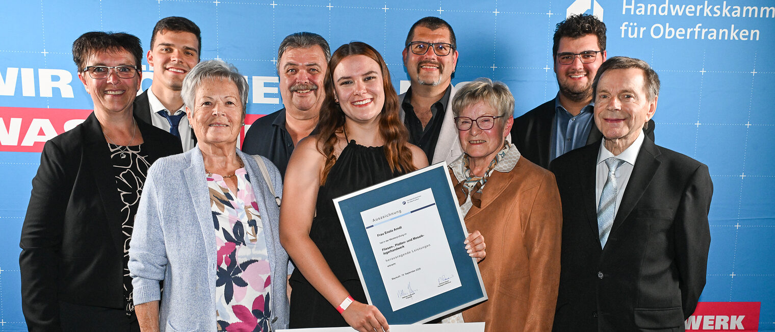 Jungmeisterin Enola Arndt posiert mit ihrer Familie vor einer Fotowand.