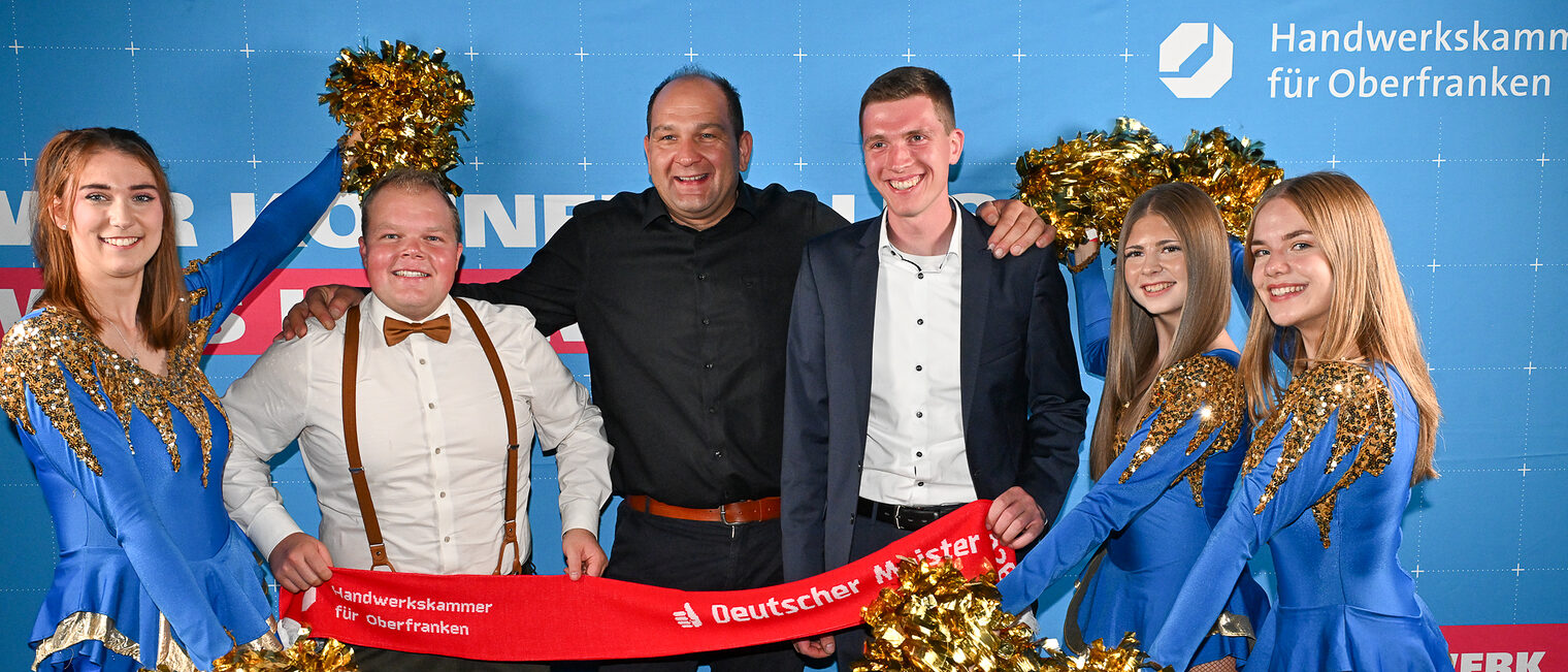 Ein Jungmeister posiert mit seiner Familie und Cheerleadern vor einer Fotowand.