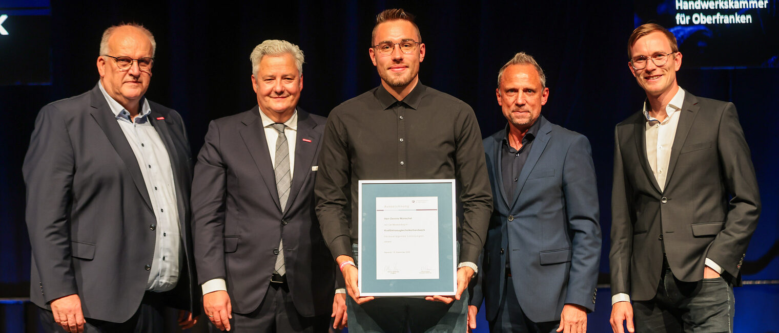 Jungmeister Dennis Wunschel präsentiert seine Ehrenurkunde mit Gratulanten auf der Bühne.