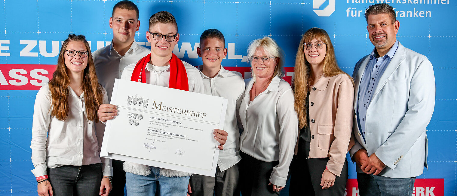 Jungmeister Christoph Weberpals posiert mit seiner Familie vor der Fotowand.