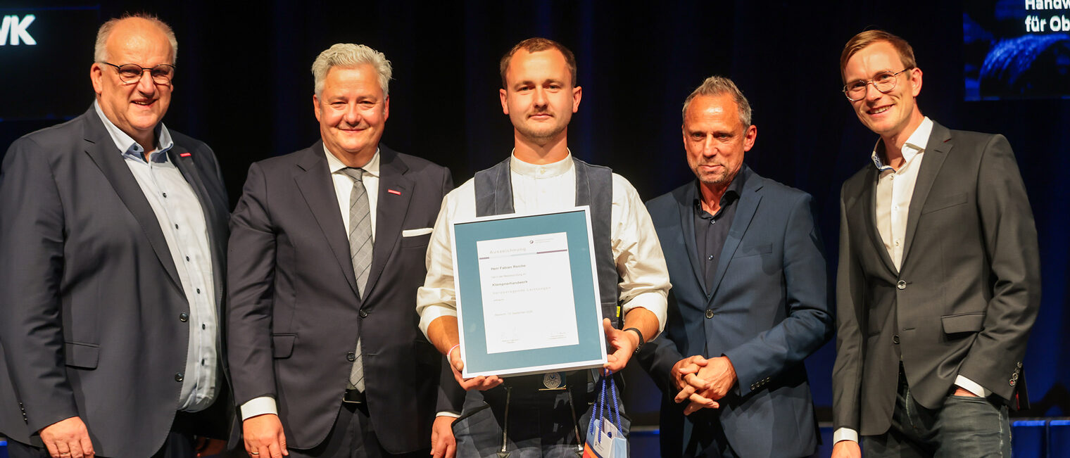 Fabian Reiche zeigt seinen Meisterbrief auf der Bühne mit Gratulanten. 