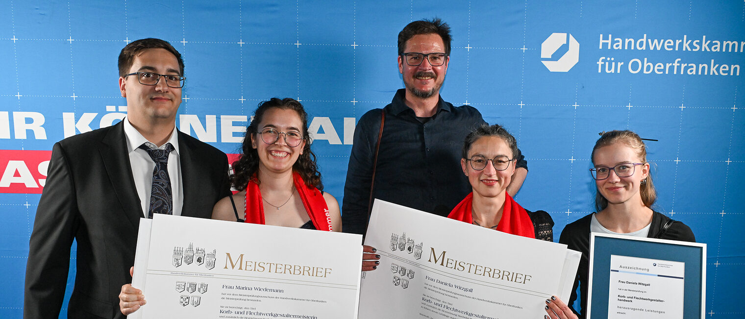 Die Jungmeisterinnen Marina Wiedemann und Daniela Witzgall posieren mit ihren Familien vor einer Fotowand.
