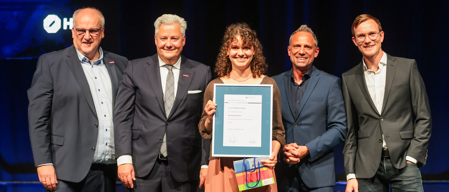Die Prüfungsbeste Friederike Hüppe steht mit ihrer Urkunde und Gratulanten auf der Bühne.