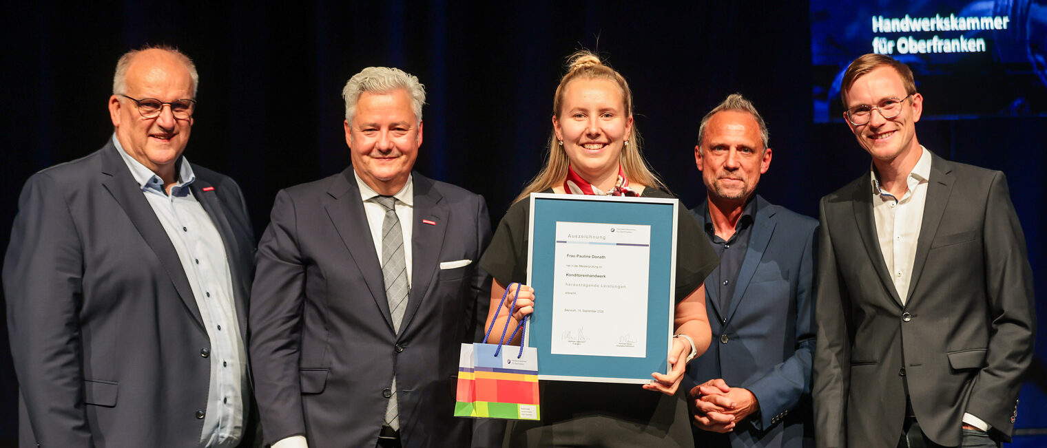 Die Prüfungsbeste Pauline Donath präsentiert ihre Urkunde mit Gratulanten auf der Bühne.