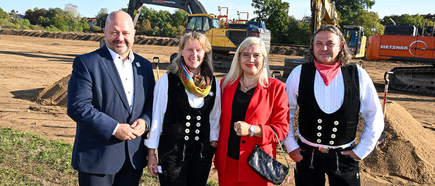 Melanie Huml und Ehrengäste aus dem Handwerk stehen für ein Gruppenfoto vor einem Bagger zusammen.