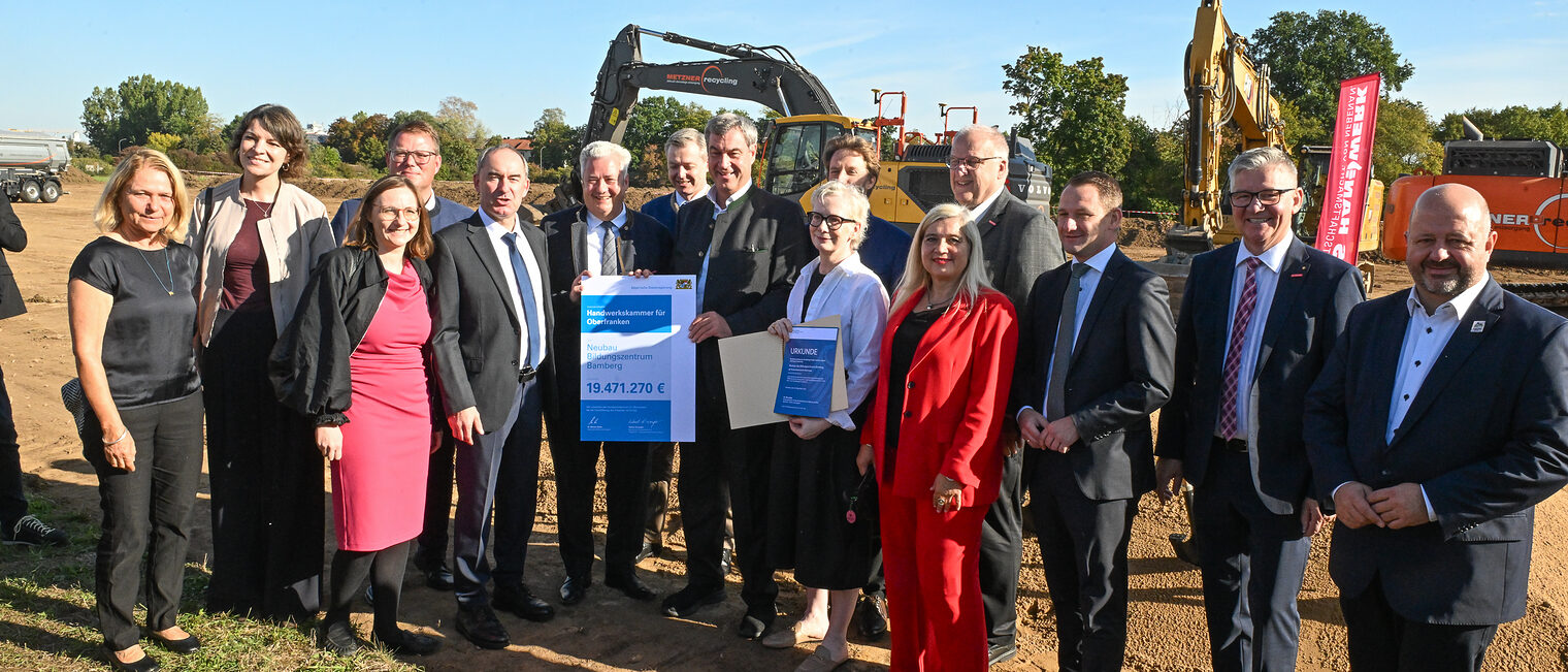 Die Ehrengäste der Baustartfeier stehen für ein Gruppenbild vor einem Bagger. 
