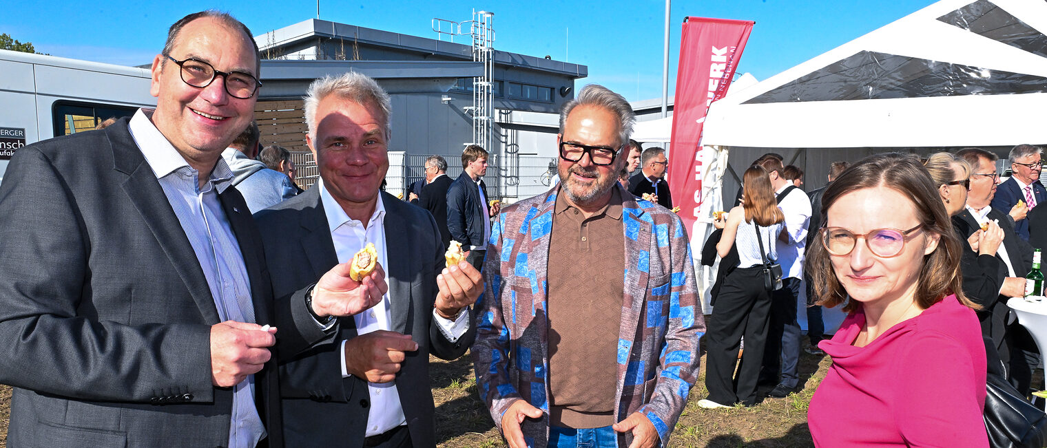 Gäste der Baustartfeier stehen an Tischen zusammen.