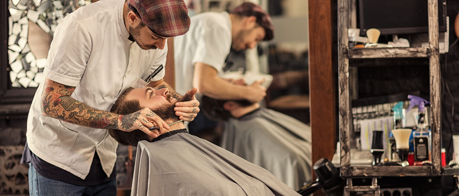 Ein Barber trimmt einem Kunden den Bart in einem Barbershop.