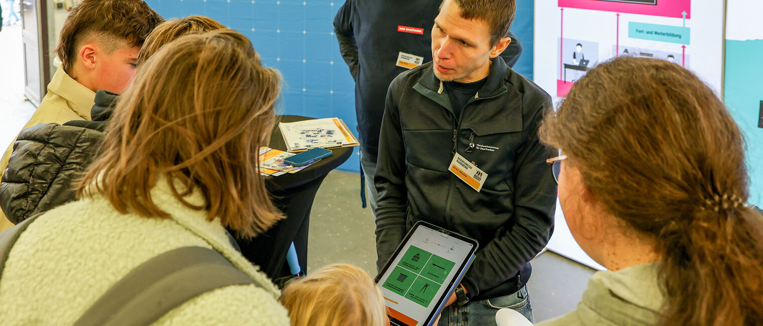 Jugendliche informieren sich an einem Stand der Nachwuchswerbung der HWK über den Berufe Checker auf einem Tablet.