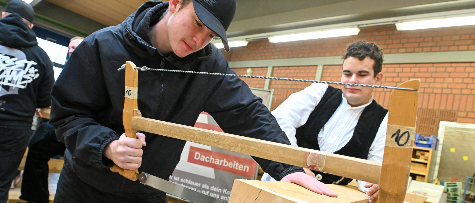 Ein Jugendlicher sägt einen Holzblock mit einer Säge zurecht.