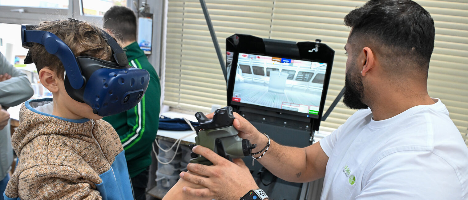Ein Jugendlicher mit VR-Brille lackiert unter Anleitung digital ein Fahrzeug.
