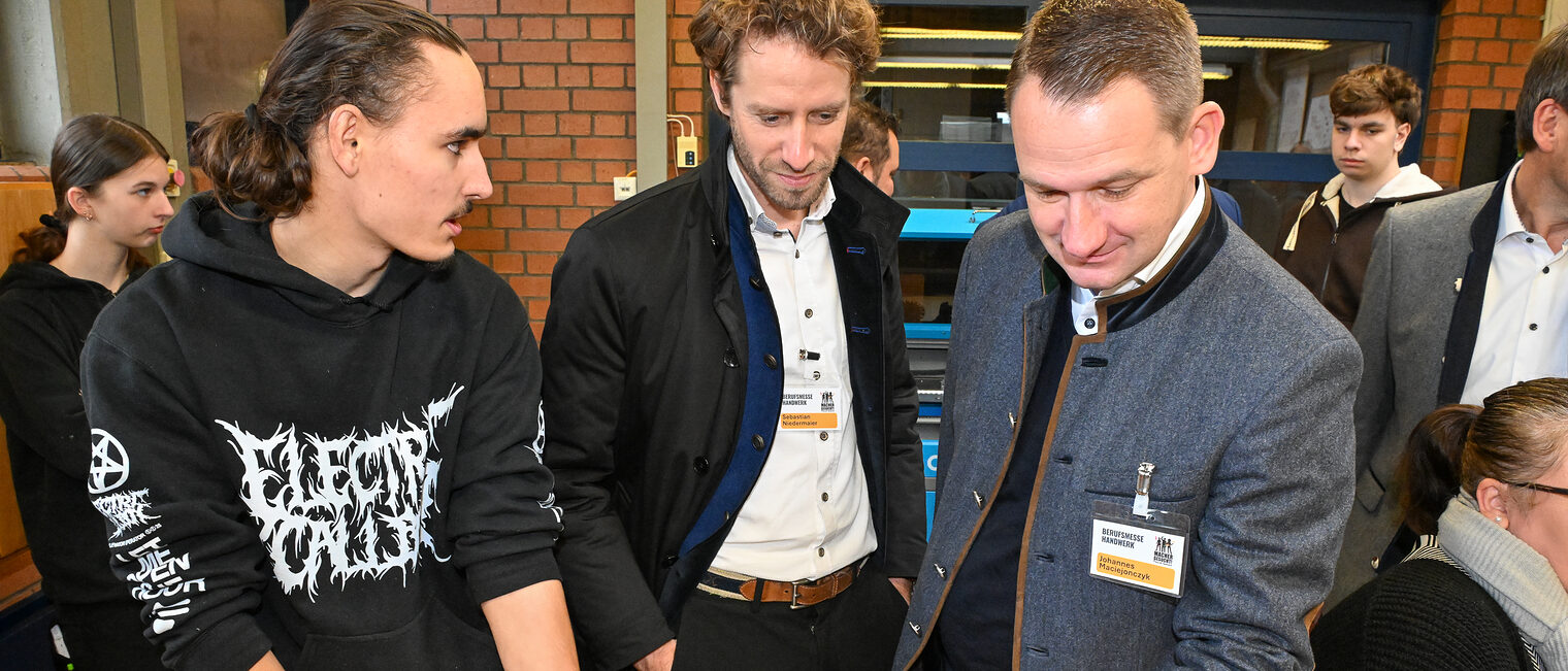 Die Ehrengäste Sebastian Niedermaier und Johannes Maciejoncyk sehen sich an einem Stand aus dem Schreinerhandwerk um.