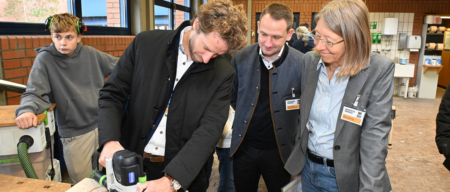 Sebastian Niedermaier fräst ein Loch in ein Holzbrett, während Johannes Maciejonczyk und Maria Emig zusehen. 