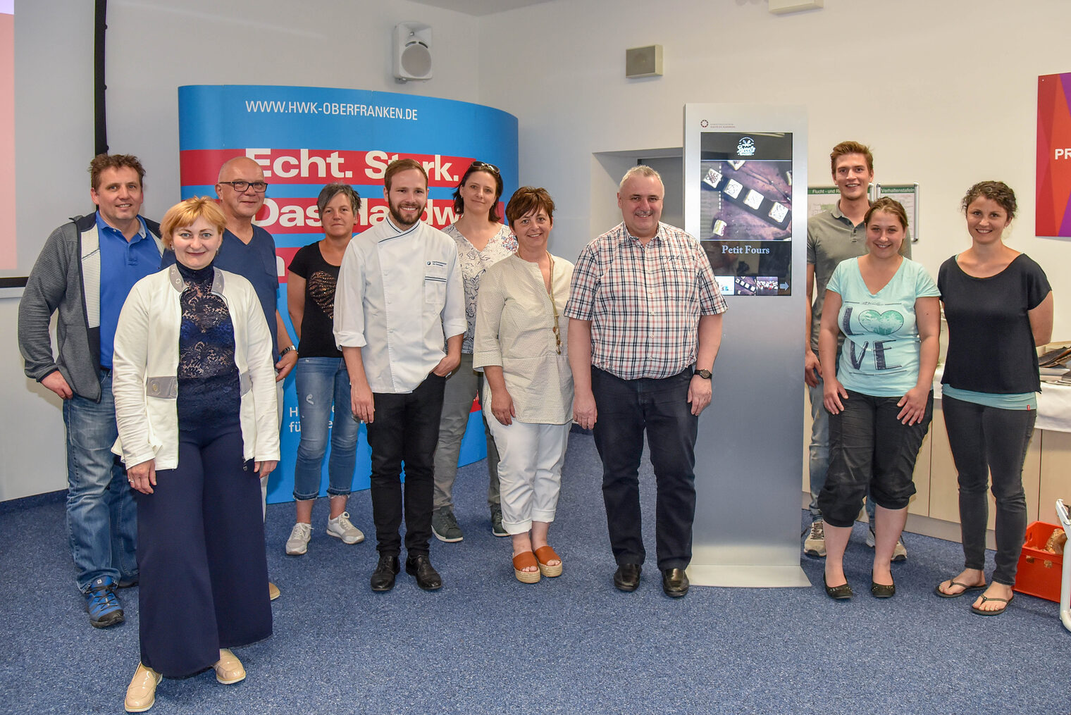 Gruppenbild mit digitaler Stele: Die Teilnehmer der Schulung machten eigene Bilder und präsentierten diese dann inklusive Text auf einem digitalen Ausgabegerät.