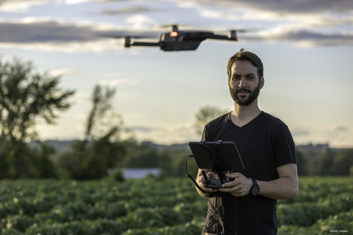 Beliebtes Spielzeug, aber auch geeignetes Werkzeug ¿ gerade für Handwerker bieten Multicopter vielfältige Chancen. Man Pilot Using a Drone Remote Controller with a digital tablet at Sunset in a field.