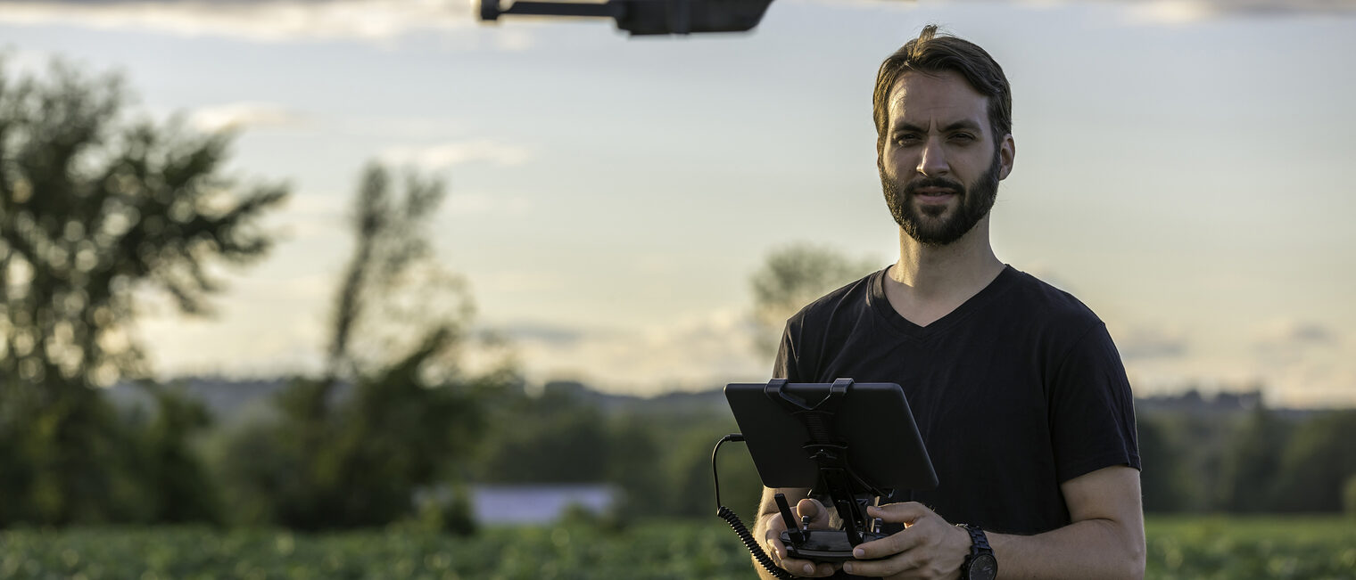 Beliebtes Spielzeug, aber auch geeignetes Werkzeug ¿ gerade für Handwerker bieten Multicopter vielfältige Chancen. Man Pilot Using a Drone Remote Controller with a digital tablet at Sunset in a field.