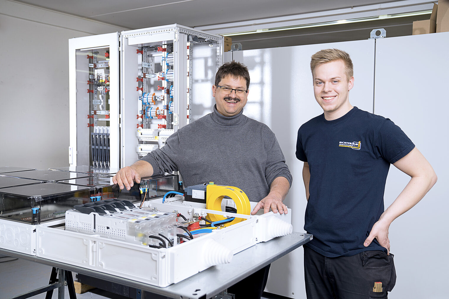 Bernd Zeilmann (im Bild links), Geschäftsführer der Richter R&W Steuerungstechnik GmbH in Ahorntal, und Sebastian Regus, Ausbildungsmeister und Montageleiter, präsentieren Komponenten für den intelligenten Energieknoten (IEK). Für das Baukastensysten stehen verschiedene Module zur Verfügung, unter anderem ein iMSys- und Einspeisemodul (iMSys: intelligentes Messmodul, im Bildvordergrund liegend) und ein Niederspannnungsverteilermodul (im Bildhintergrund stehend). Schlagwort(e): Energiewende, IeK, Intelligenter Energieknoten, DC-Netze, Gleichstrom, iSyme, intelligente Symmetrieeinrichtung, iMSys, Modulare Steuereinheit, DC-Grid-Manager, Seifriz-Preis, R&W Steuerungstechnik, Universität Bayreuth, HWK Oberfranken, Fraunhofer IISB