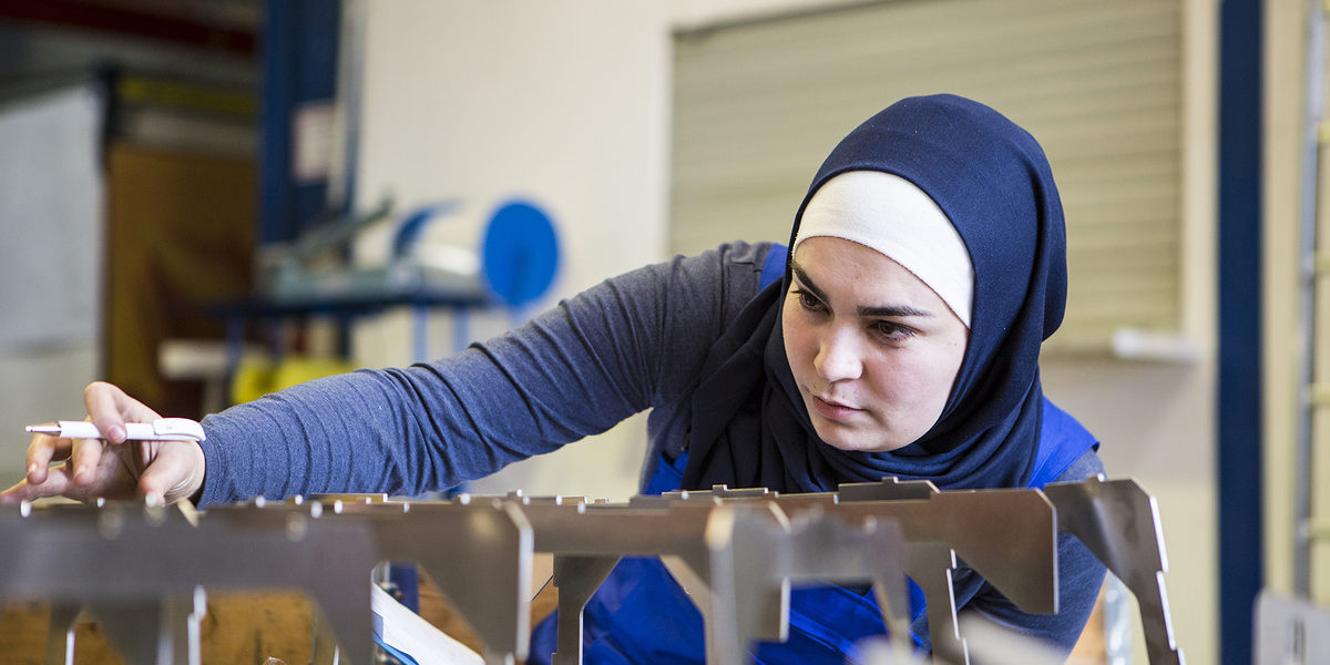 Young female trainee makes a quality control of metal pieces