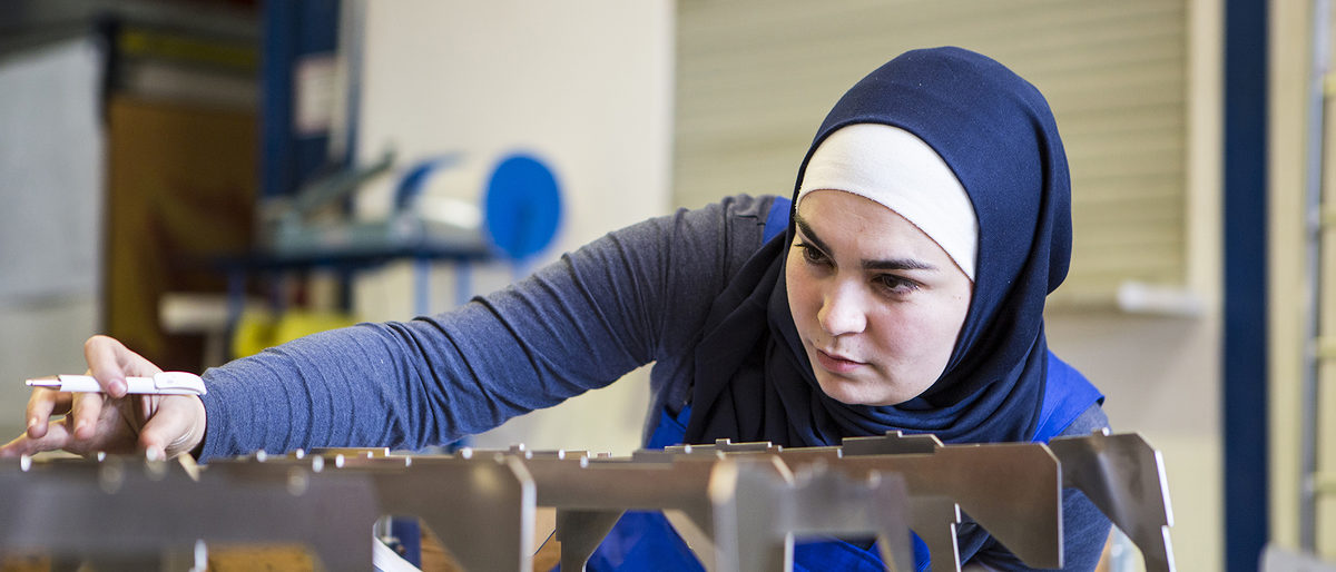 Young female trainee makes a quality control of metal pieces